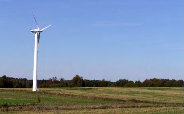 Bild på ett vindkraftverk på en slätt med grönt gräs och klarblå himmel.
