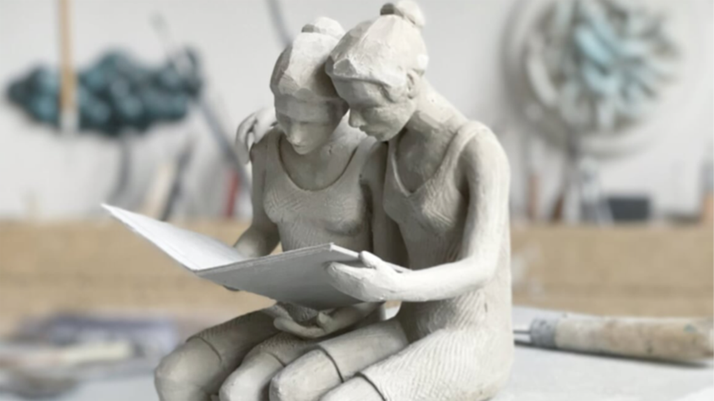 Konstverk av två flickor i vad som ser ut som betong. De sitter lutade mot varandra och läser i en stor bok eller i tidning ihop.